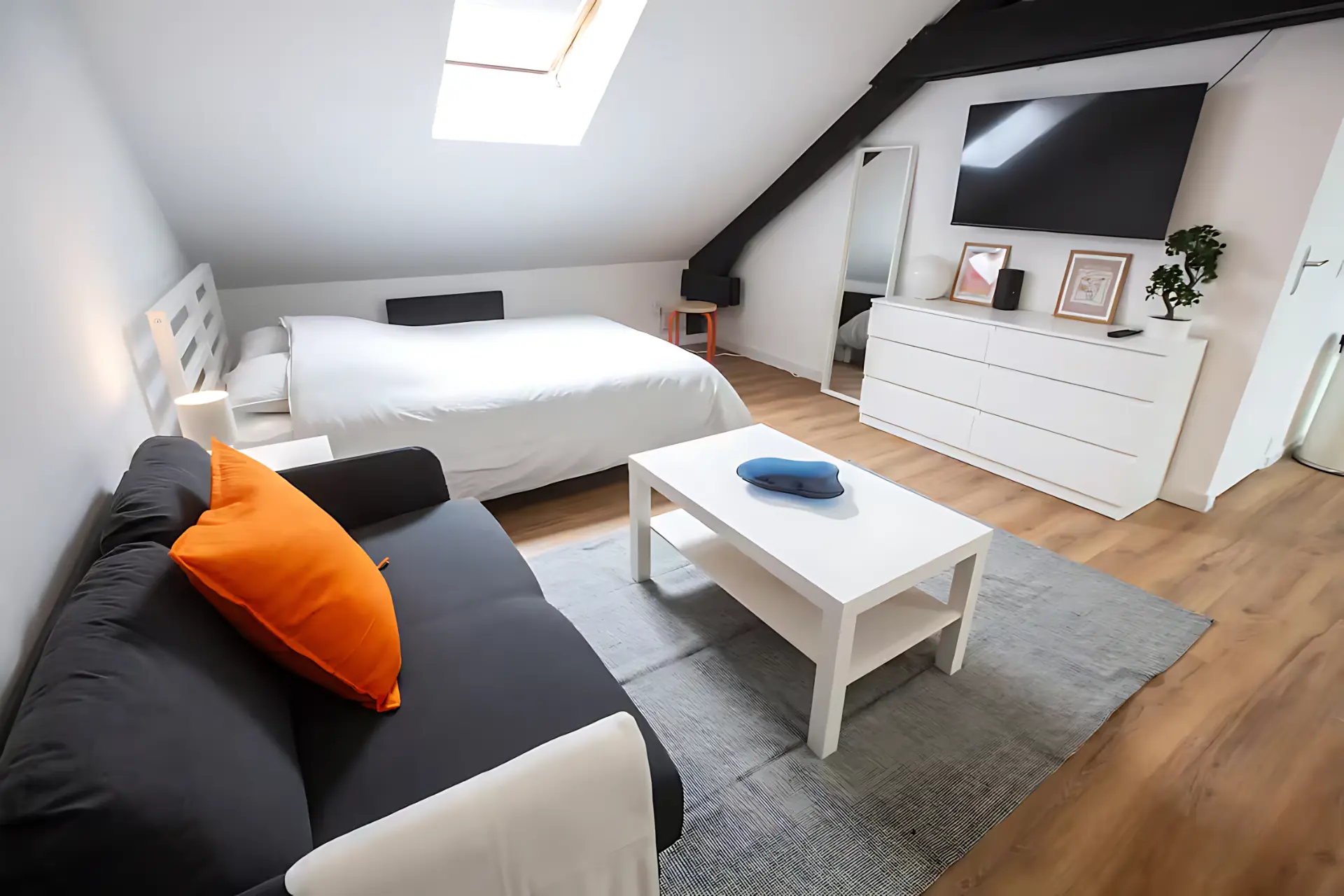 Pièce de vie sous combles aménagée avec canapé, lit et parquet