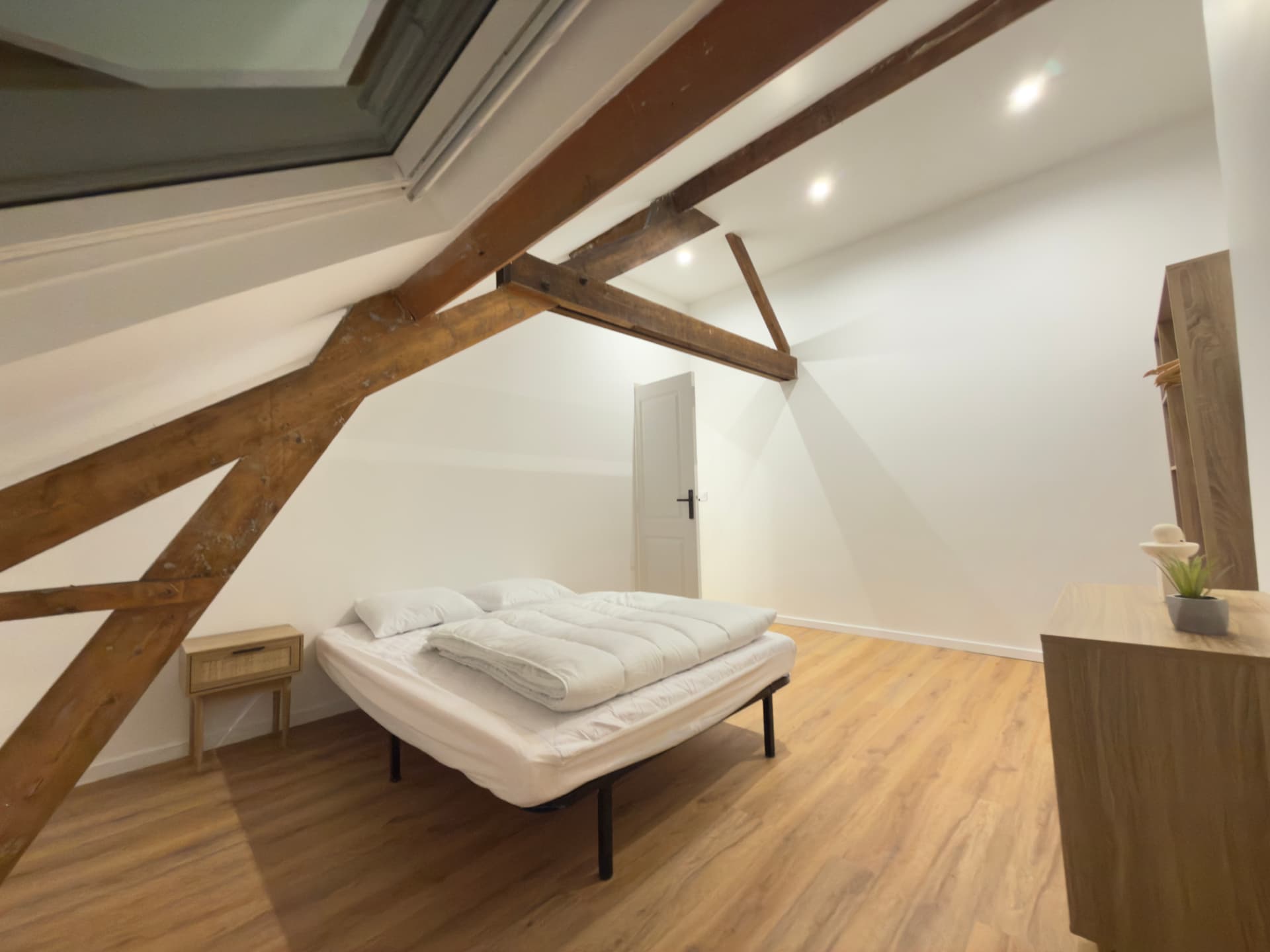 Chambre mansardée aux poutres apparentes lasurées et velux