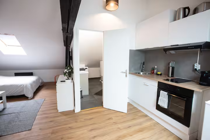 Kitchenette blanche et coin nuit dans un studio sous combles