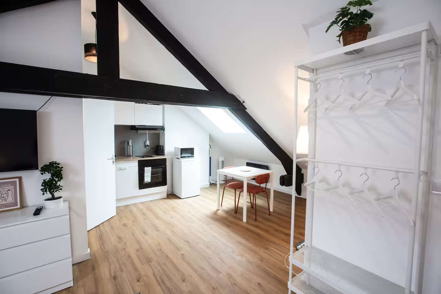 Studio sous combles aménagé avec kitchenette blanche et poutres noires
